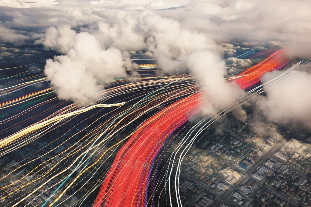 A city view from above showing clouds, the city landscape, and coloured light trails that represent technology