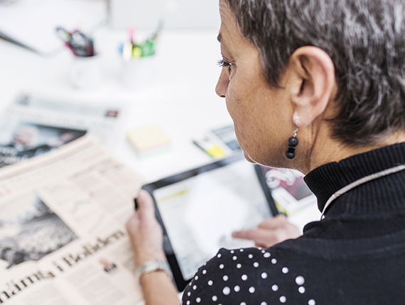 Cropped image of businesswoman using digital tablet with newspapers on desk