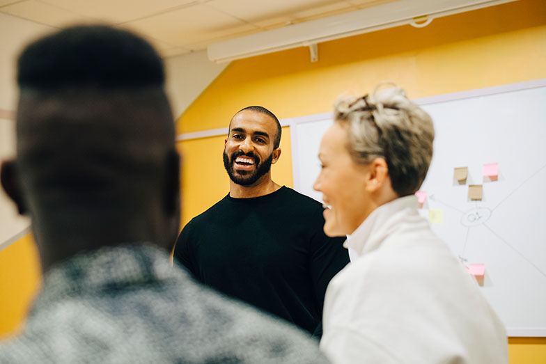 Three people laughing in front of a whiteboard