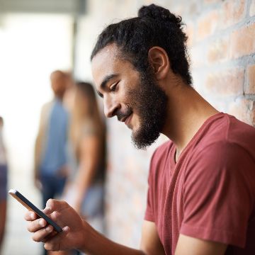 Shot of a young person standing in a hallway using a cellphone with friends in the background