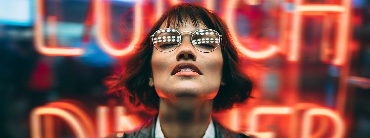 Girl with glasses looking upwards in front of neon lights