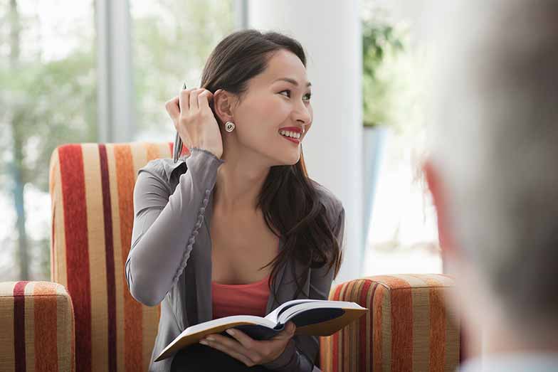 woman holding a book and touching her hair while smiling