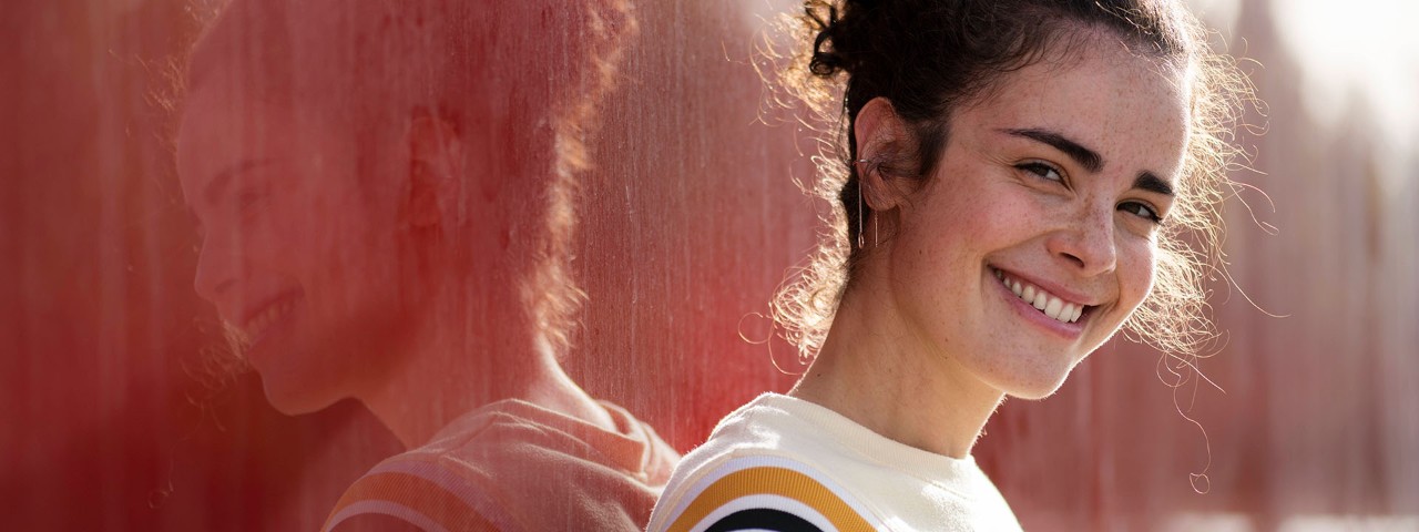 smiling young persons standing in front of reflective wall