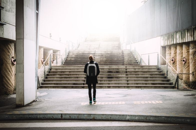 person wearing backpack looking upwards into wide industrial staircase