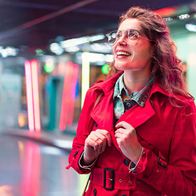Person in a red coat at train station smiling skywards 
