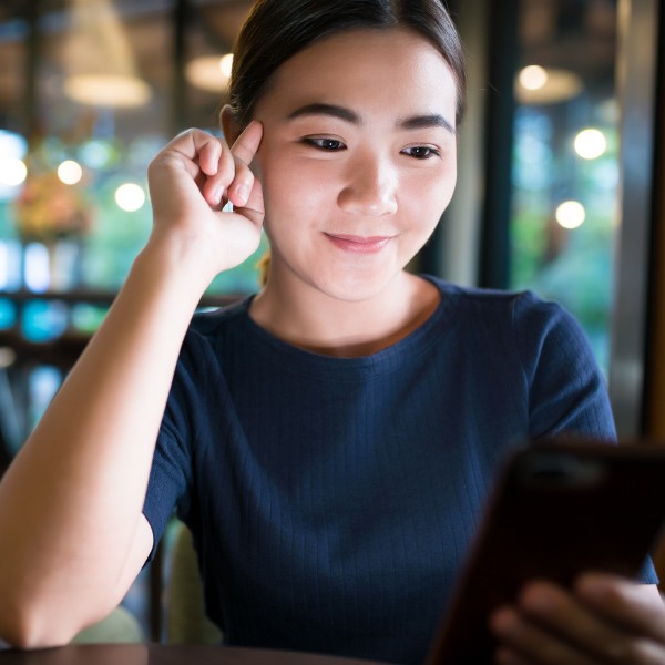 PORTRAIT OF SMILING YOUNG WOMAN USING MOBILE PHONE IN BATHROOM