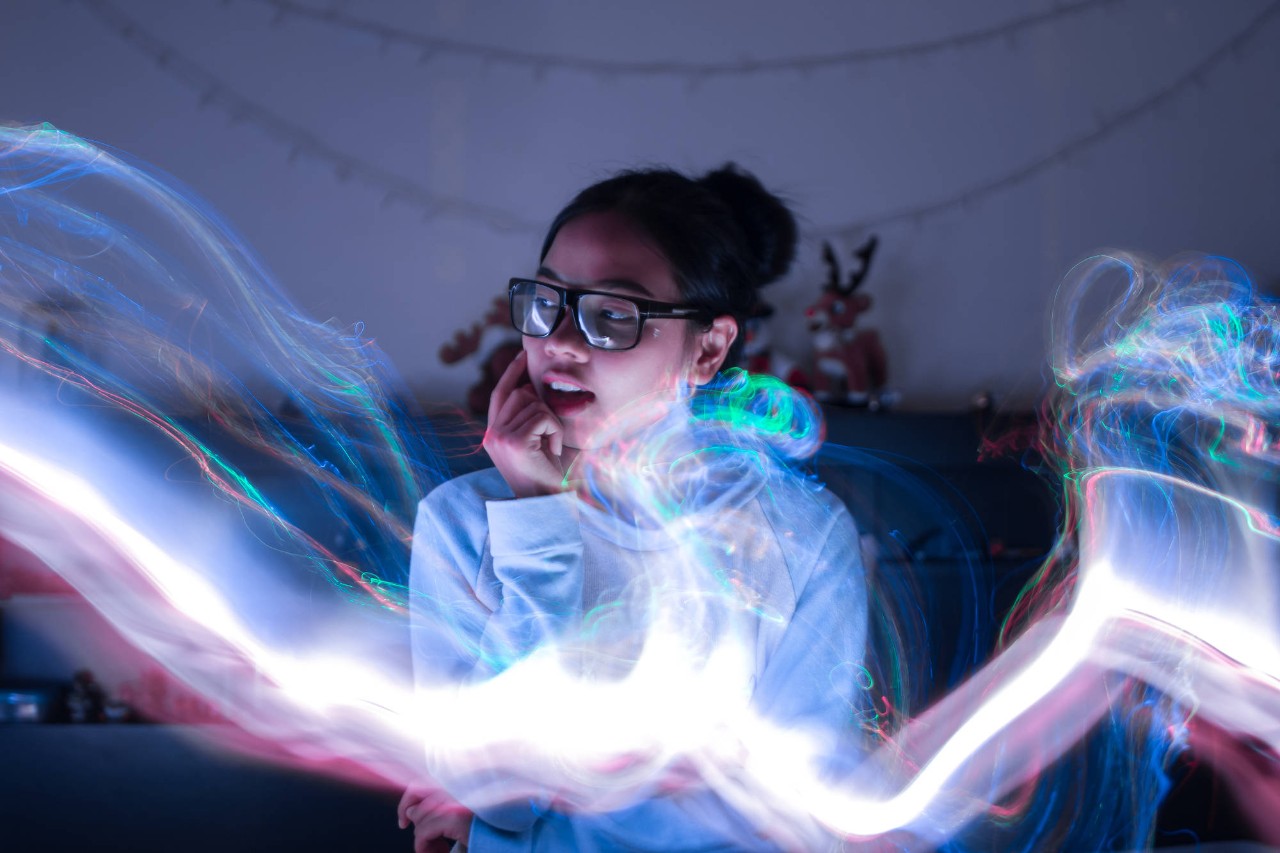 CLOSE-UP OF YOUNG WOMAN WITH EYEGLASSES IN ILLUMINATED NIGHTCLUB