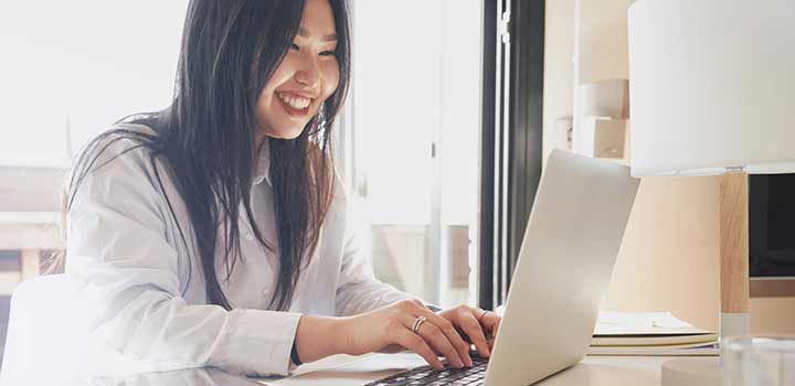 A student working happily at their laptop in a sun-filled room