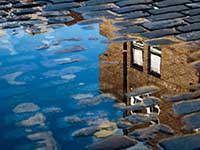 Housing reflected in a puddle on a cobbled street
