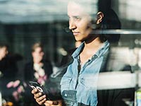 Someone standing behind a window, looking at their mobile phone