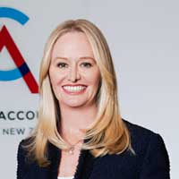 Photo of Ainslie Van Onselen, Chief Executive of CA ANZ. Ainslie is looking to the camera and smiling, in front of a backdrop showing a partial CA ANZ logo. 