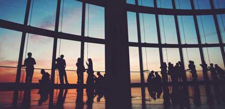Silhouette image of a group of people in a large modern building with floor to ceiling windows at dusk.