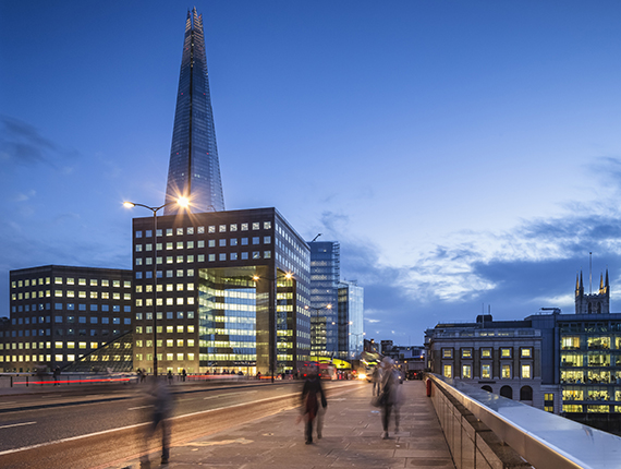 Image of a London bridge, skyscrapers and the shard around and people walking on the bridge but shown as blurred