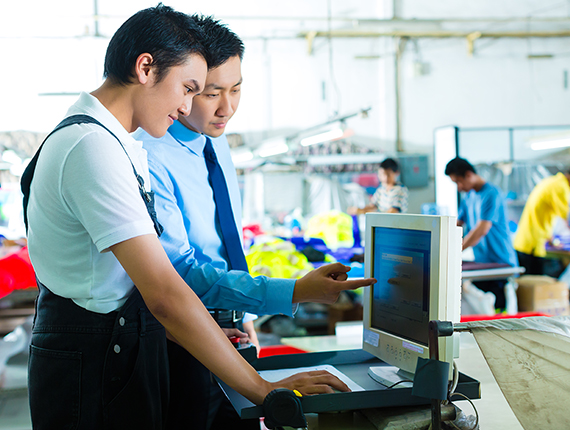 Two south east Asian men standing looking at a computer screen on a factory room floor