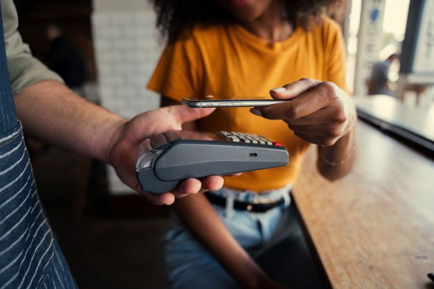 Image of person in orange tshirt holding a credit card over a contactless payment device