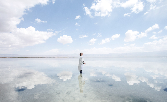 Image on the cover of the report of a woman on her own, in the water on a beach on a cloudy day with the clouds reflected in the water 