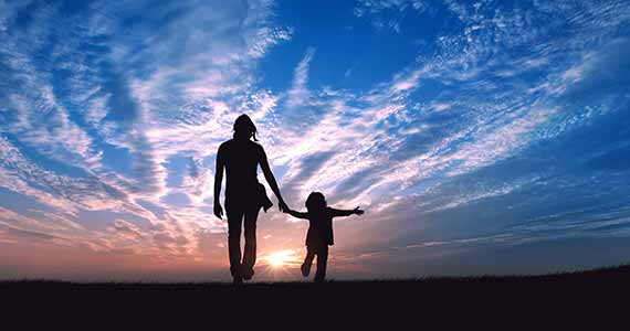 Mother and child walking towards the horizon at sunset