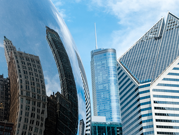 Image of Skyscrapers, half of skyscrapers are seen against a blue sky and the other half are seen via a reflective object