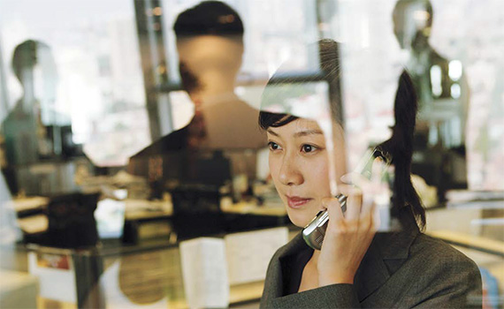 Image of a female Asian professional standing by an office window talking on the mobile phone