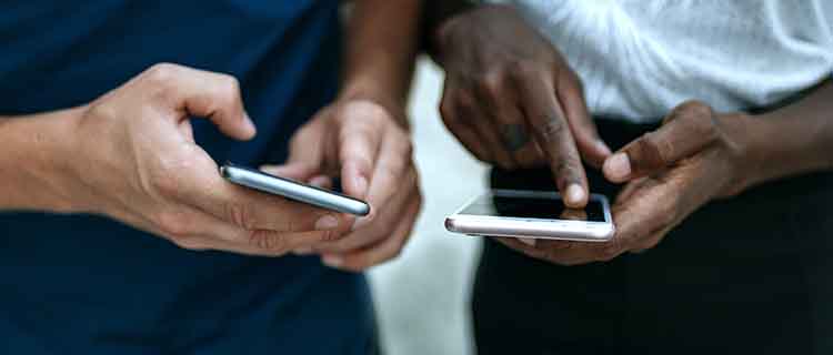 Mid section showing the hands of two men, one light skinned and one dark skinned, touching mobile phone screens