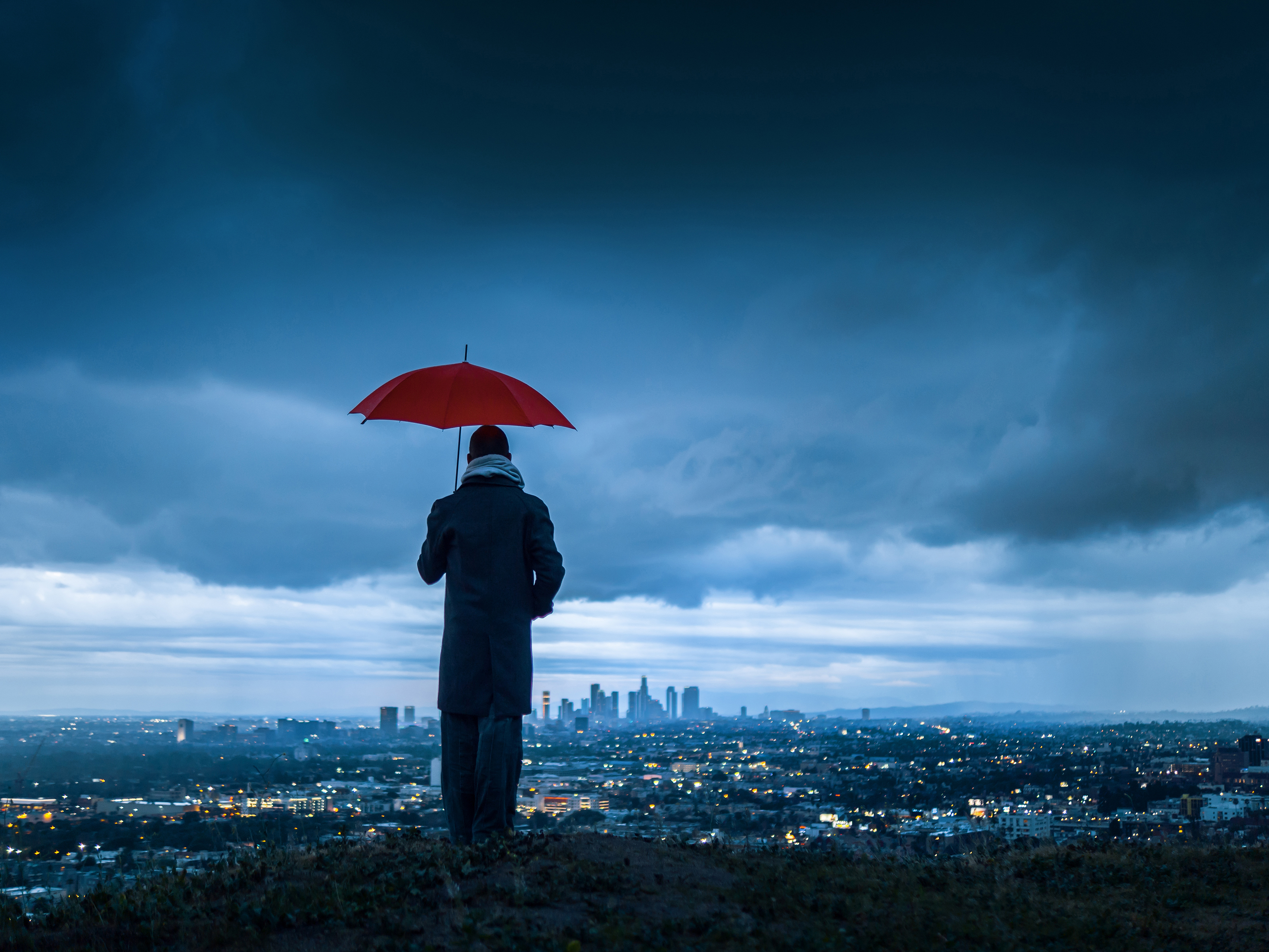 Image on the cover of the report featuring a man holding a red umbrella at the top of a hill and looking down at a city at dusk. 