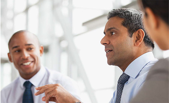 Image of two men both wearing a shirt and tie, sitting and talking