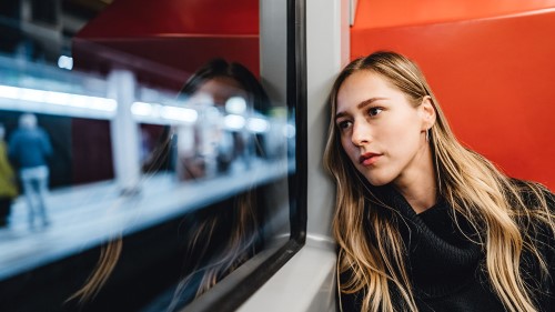 Image of a girl sat on a train carriage next to a window overlooking a station platform