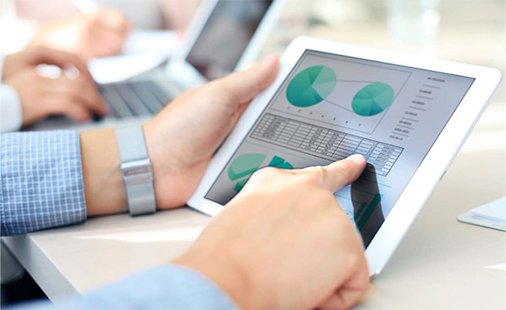 The hands of a man holding a digital mobile tablet. On the tablet screen are two pie charts and tables with data/numbers