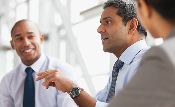 Image of two men, both wearing a shirt and tie sitting and talking 