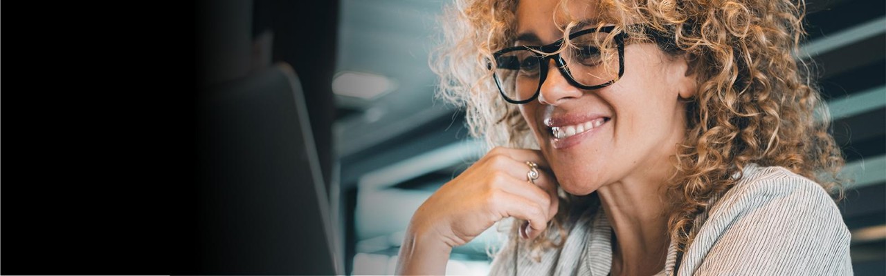 Person with curly hair and thick framed glasses working happily on computer screen