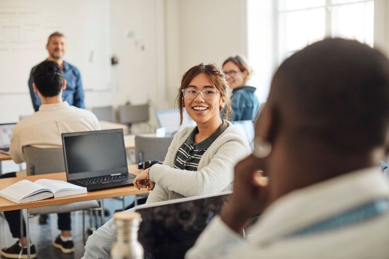 Happy student in classroom with laptop and textbook open