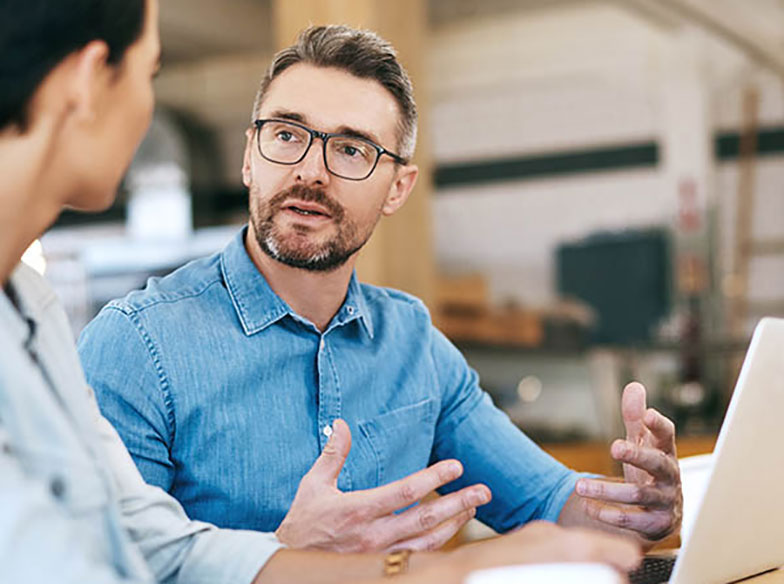 Person in an office, face-on to camera talking to another person who is facing them