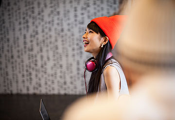 young person wearing beanie hat and headphones smiling skywards 
