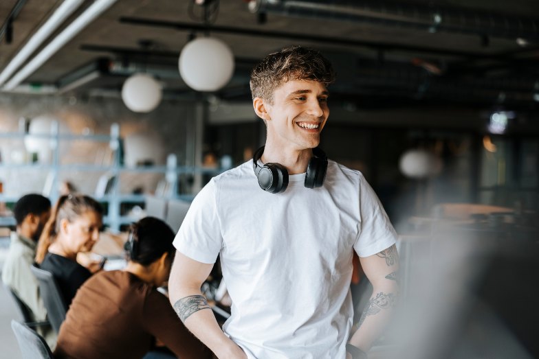 happy young person with earphones around neck with students sitting in background