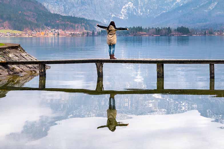 person on a jetty over a lake with arms spread wide