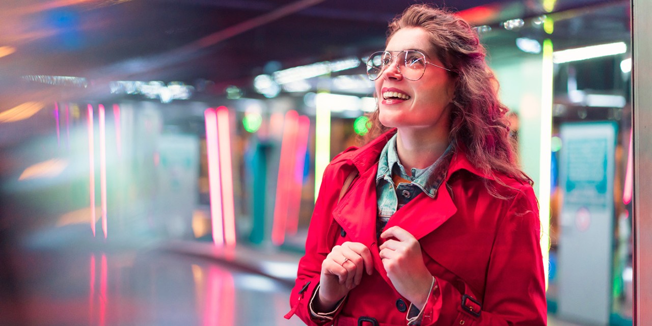 Person in spectacles and red coat smiling with colourful background