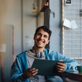 Happy person using a tablet and drinking coffee in urban office or cafe