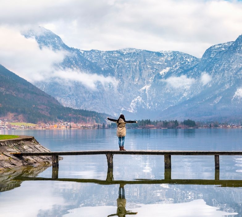 Holiday destinations theme image of a woman with open arms enjoying the lovely Hallstatter lake and the peaks of the Dachstein Mountains, in Hallstatt, Austria.