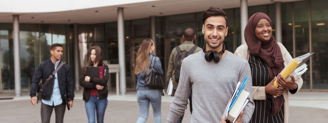 young people carrying books leaving building