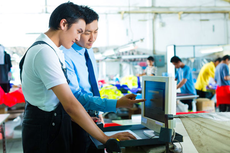 two persons looking at a computer screen with a factory in the background