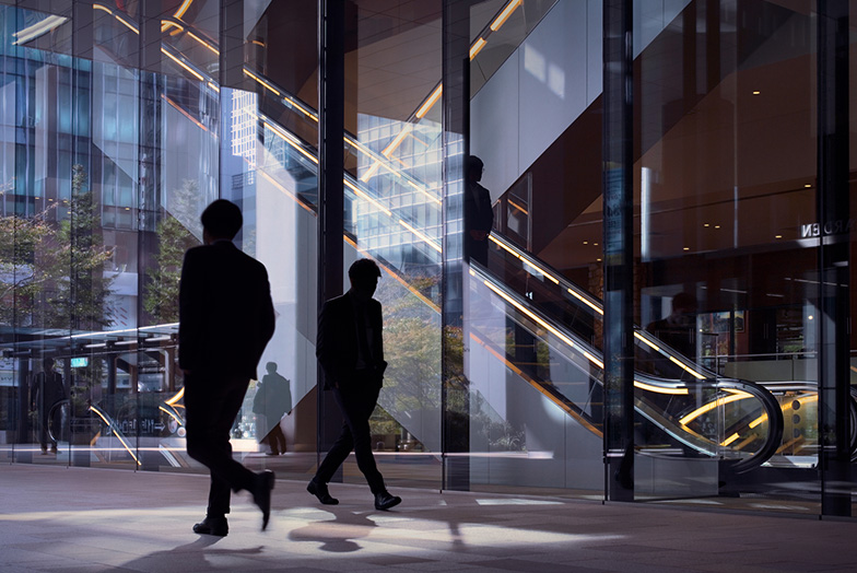 Two people walking past a glass wall, next to an escalator