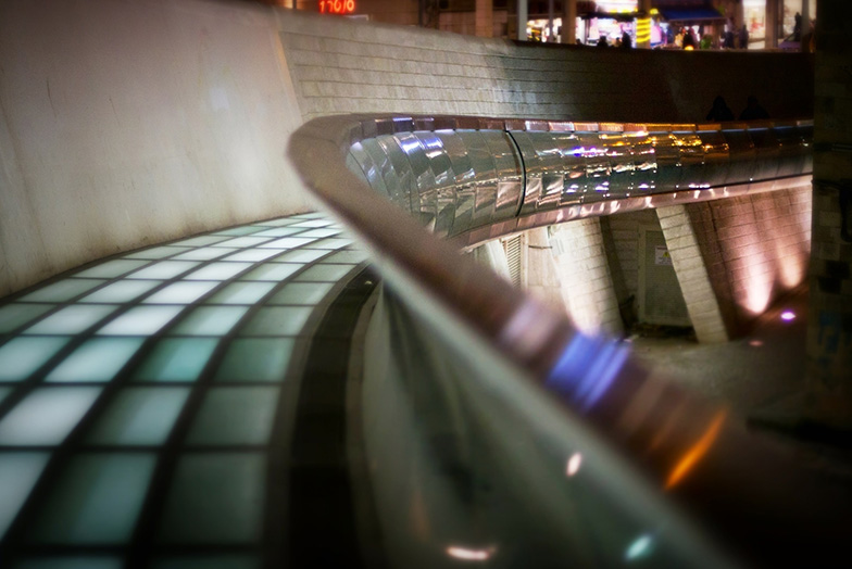 A night view of a curved, raised walkway of glass and stone