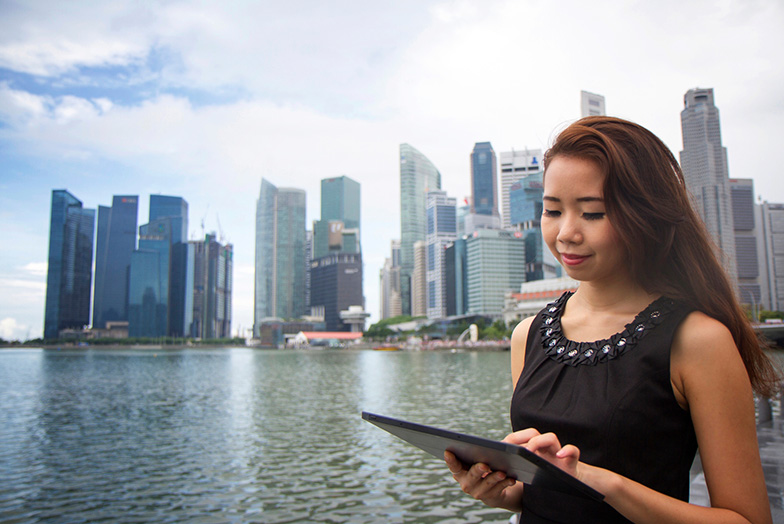 Person using tablet in front of stretch of water and cityscape 