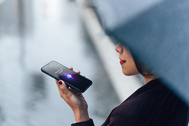 Person speaking to an AI assistant on a rain spattered mobile phone. Part of an umbrella is obscuring their face.