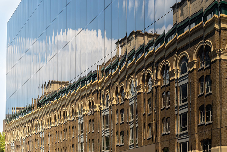 A sandstone building reflected onto a glass building