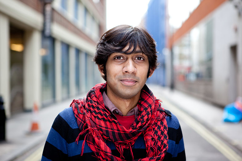 young person wearing scarf standing in street smiling to camera