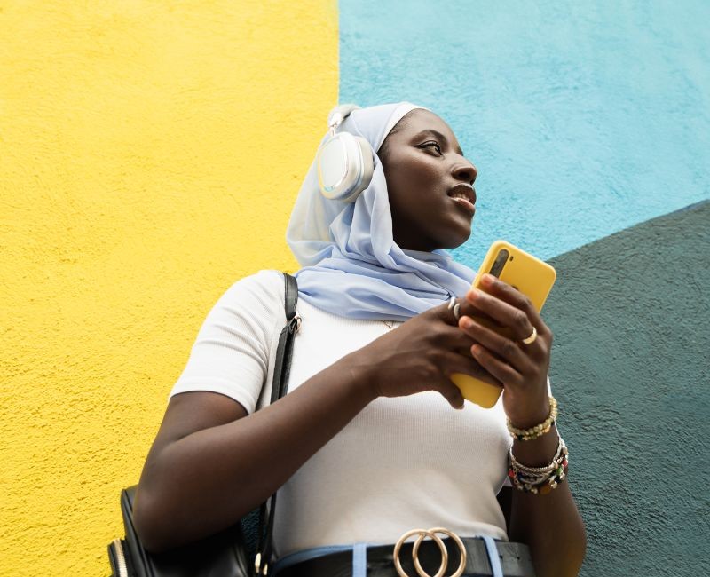 person-wearing-hijab-and-earphones in front of colourful painted wall