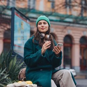 young pernso wearing beanie and headphones sitting outside a university bus stop