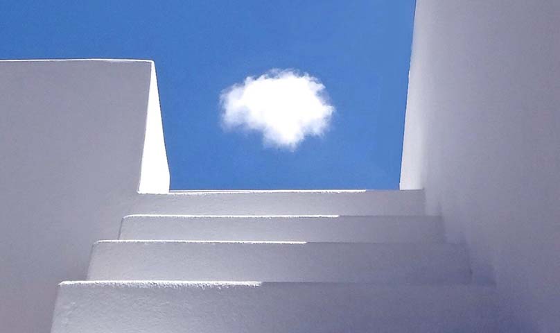 a single white fluffy cloud framed against a blue sky by white steps and walls