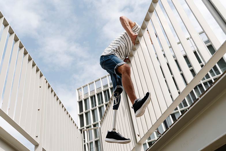person with one artificial leg jumping over a railing